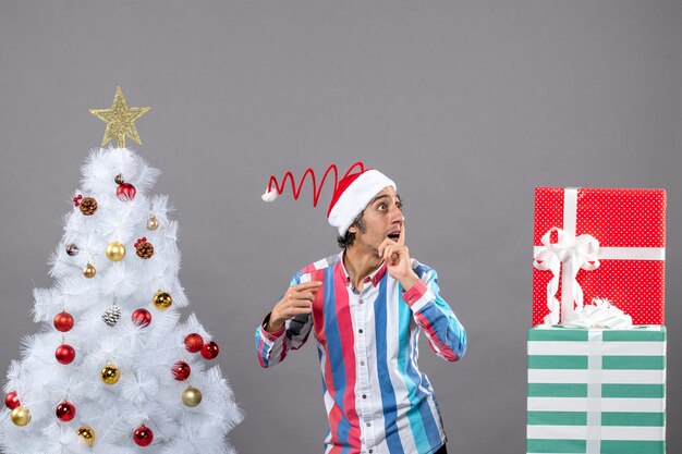 Hombre curioso de vista frontal observando algo parado cerca del árbol de Navidad blanco