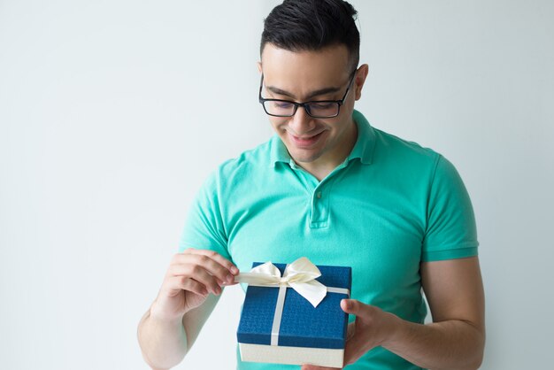 Hombre curioso vistiendo polo camiseta y desenvolviendo caja de regalo