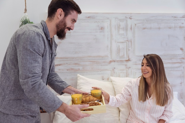 Hombre dando bandeja con desayuno romántico a mujer.