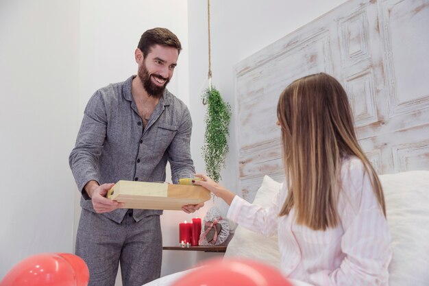 Hombre dando bandeja de madera con comida a mujer.