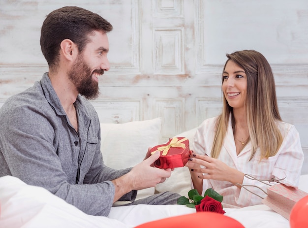 Hombre dando caja de regalo a mujer en la cama