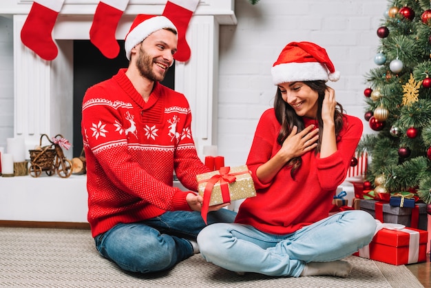 Hombre dando presente a mujer cerca de arbol de navidad.