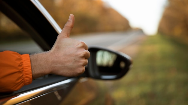 Hombre dando pulgares hacia arriba fuera de su coche durante un viaje por carretera