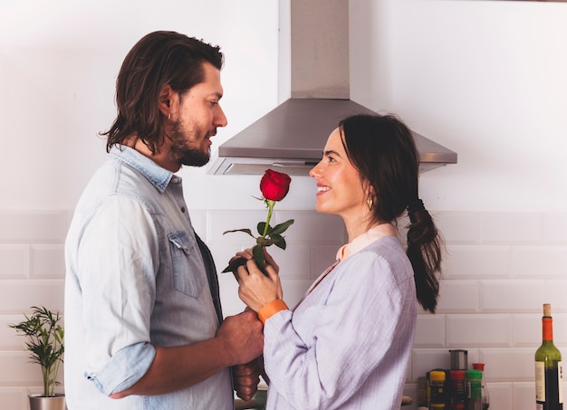 Hombre dando rosa brillante a mujer en cocina