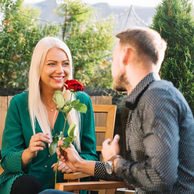 Hombre dando rosa roja a su sonriente mujer rubia joven