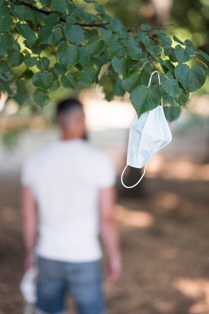 Hombre dejando su máscara médica en un árbol