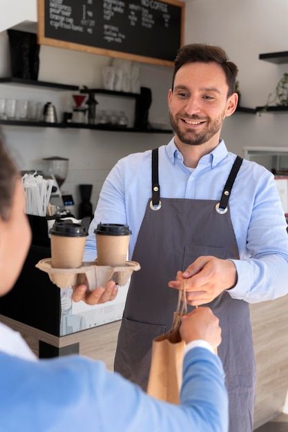 Foto gratuita hombre con delantal ofreciendo comida para llevar empaquetada a clienta