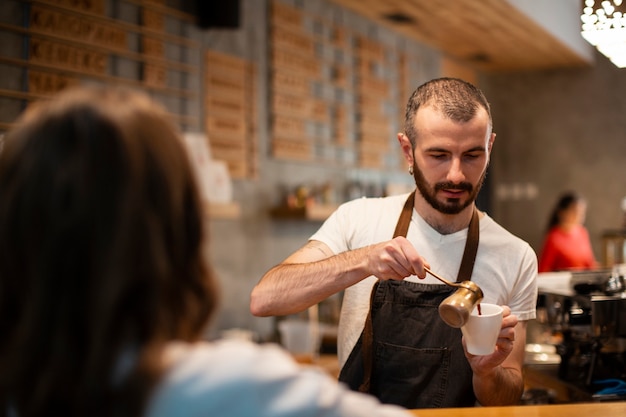 Hombre en delantal vertiendo café en taza para cliente