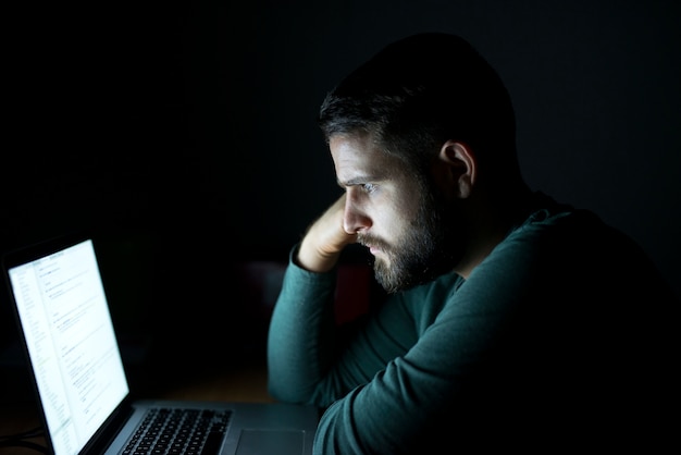 Hombre delante de la computadora portátil leyendo y concentrado