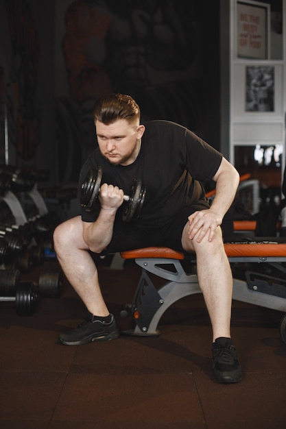 Hombre de deportes en el gimnasio. Un hombre realiza ejercicios. Chico en una camiseta