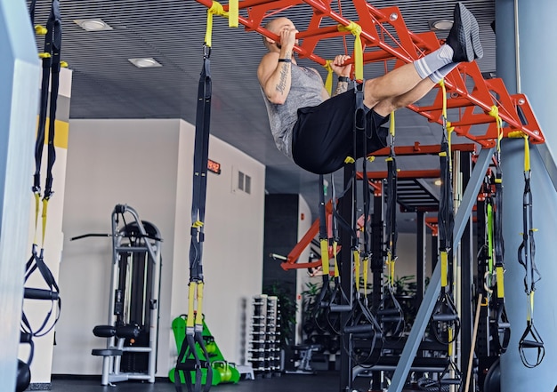 Hombre deportivo con cabeza rapada haciendo flexiones en el soporte de correas trx.