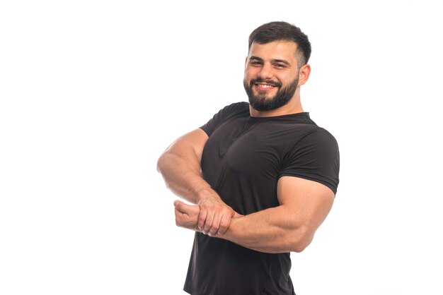 Hombre deportivo en camisa negra poniendo su mano a los músculos del brazo