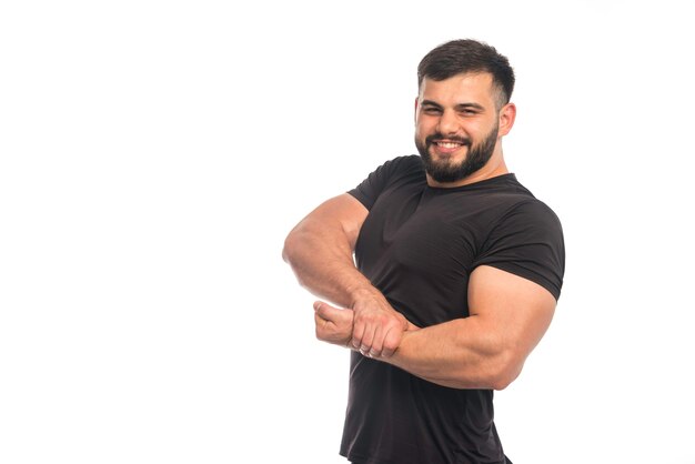 Hombre deportivo en camisa negra poniendo su mano a los músculos de su brazo.