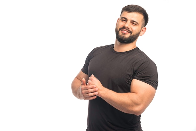 Hombre deportivo en camisa negra que demuestra los músculos de su brazo y parece positivo
