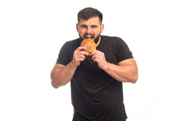 Foto gratuita hombre deportivo con camisa negra sosteniendo una rosquilla y comiendo