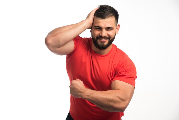 Hombre deportivo con camisa roja demostrando sus músculos.