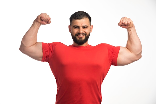 Foto gratuita hombre deportivo con camisa roja que demuestra sus músculos del brazo y parece seguro