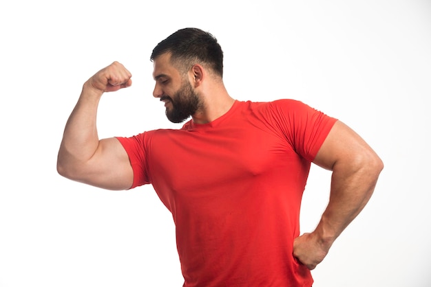 Foto gratuita hombre deportivo con camisa roja que demuestra sus músculos del brazo y parece seguro.