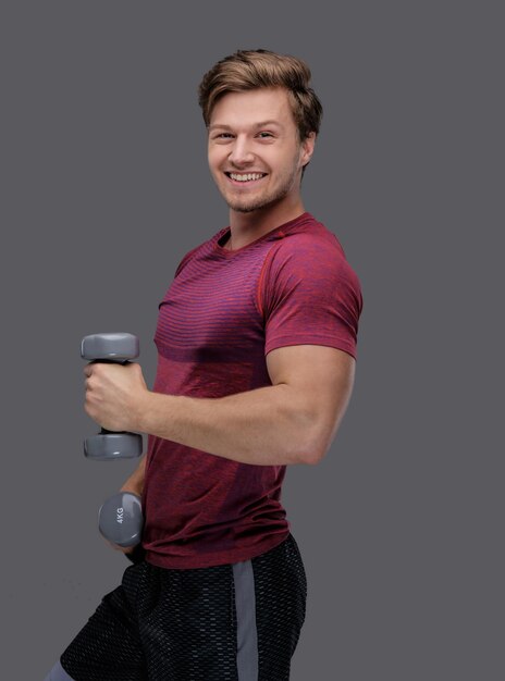 Un hombre deportivo con una camiseta roja sostiene pesas.