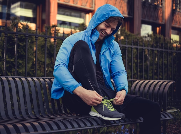 Un hombre deportivo con una chaqueta deportiva azul ata sus zapatillas.