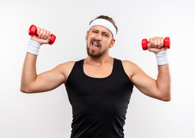 Foto gratuita hombre deportivo guapo joven confiado con diadema y muñequeras sosteniendo pesas aisladas en la pared blanca