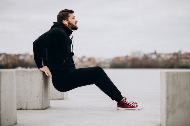 Hombre deportivo guapo que se extiende en el parque junto al río