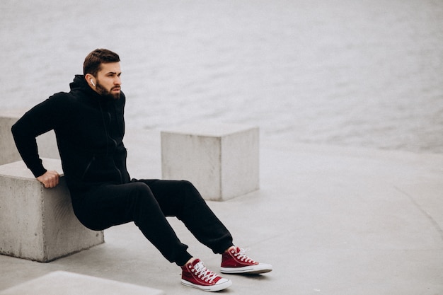 Hombre deportivo guapo que se extiende en el parque junto al río