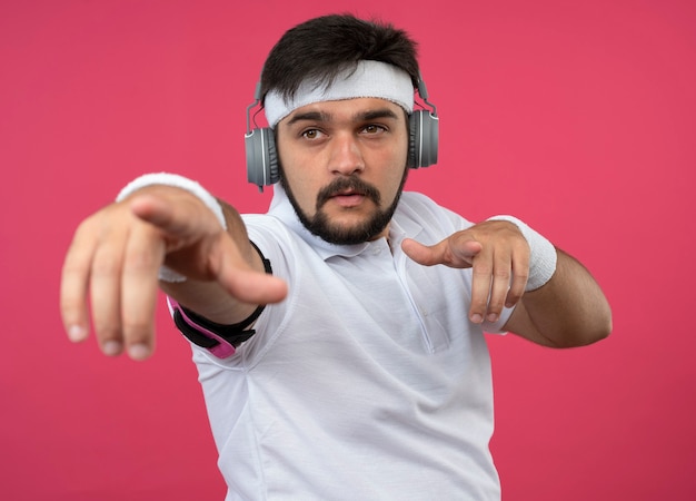 Hombre deportivo joven complacido con diadema y muñequera con auriculares y puntos de banda para el brazo del teléfono en la parte delantera