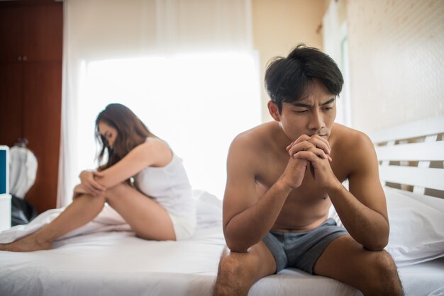 Hombre deprimido sentado en la cama en el dormitorio tiene problemas con su esposa