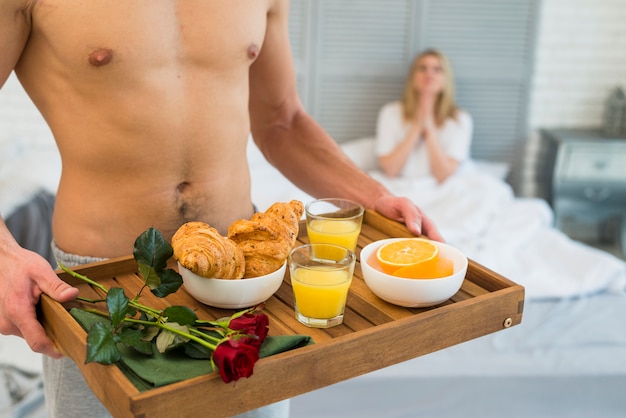 Hombre con desayuno a bordo junto a la mujer sentada en la cama