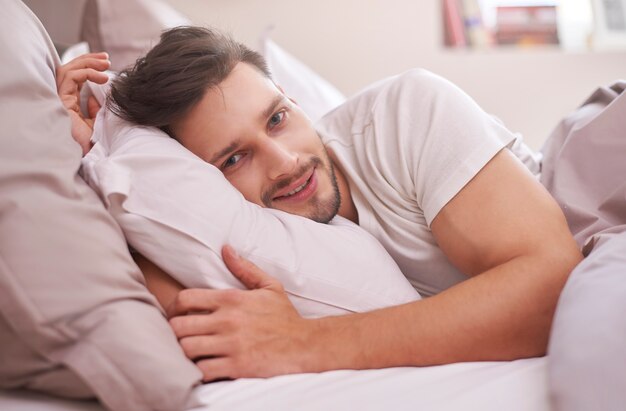 Hombre descansado acostado en su cama por la mañana