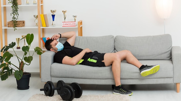 Hombre descansando en un sofá mientras usa ropa deportiva y una mascarilla