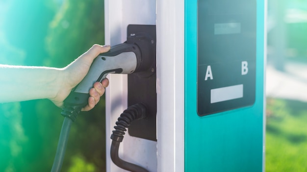 Hombre desenchufar el cargador eléctrico del muelle en la estación de carga