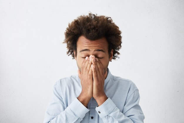 Hombre desesperado con espeso cabello oscuro que cubre su rostro con las manos cerrando los ojos está cansado