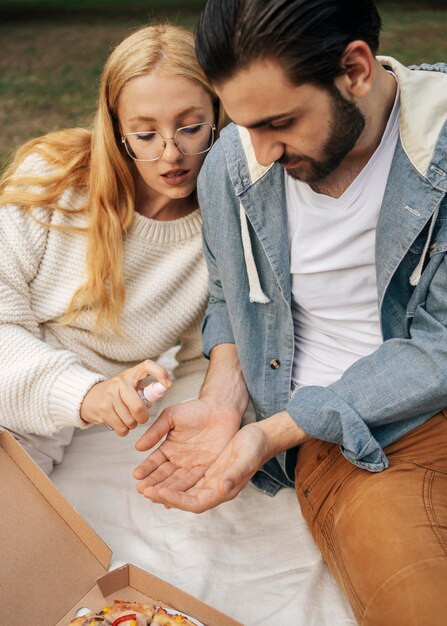 Hombre desinfectando las manos de su novia antes de hacer un picnic