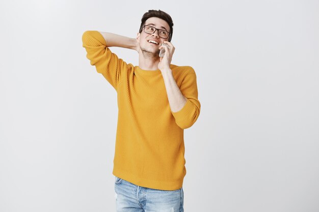 Hombre despreocupado hablando por teléfono y sonriendo incómodo