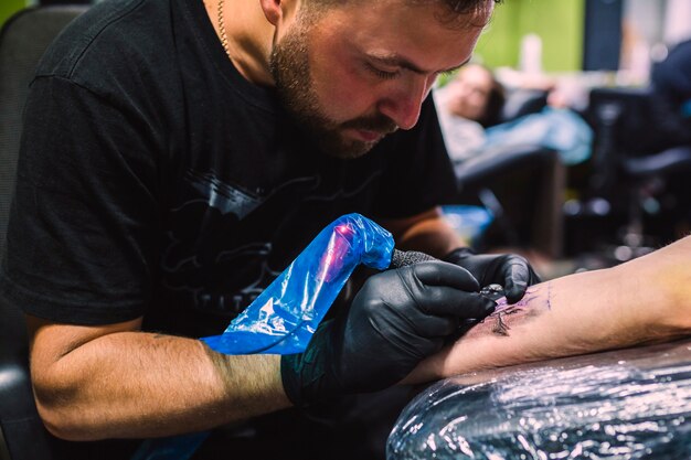 Hombre dibujando con tatuaje pluma en el brazo