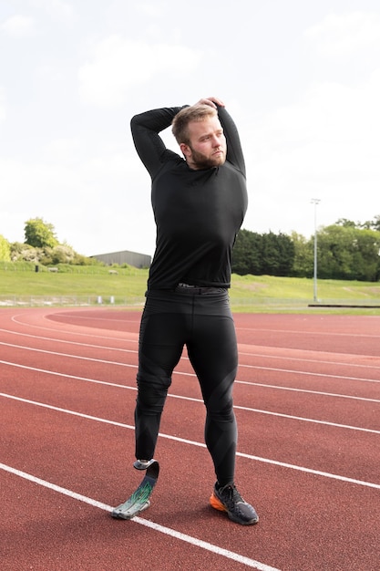 Hombre discapacitado de disparo completo que se extiende en la pista de atletismo