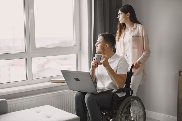 Hombre discapacitado que usa la computadora portátil en casa y trabaja de forma remota. La novia animando a su novio.