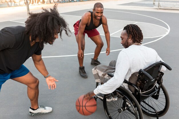 Hombre discapacitado en silla de ruedas jugando baloncesto con sus amigos