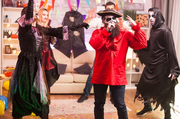 Hombre disfrazado de pirata haciendo karaoke en la fiesta de halloween con sus amigos.