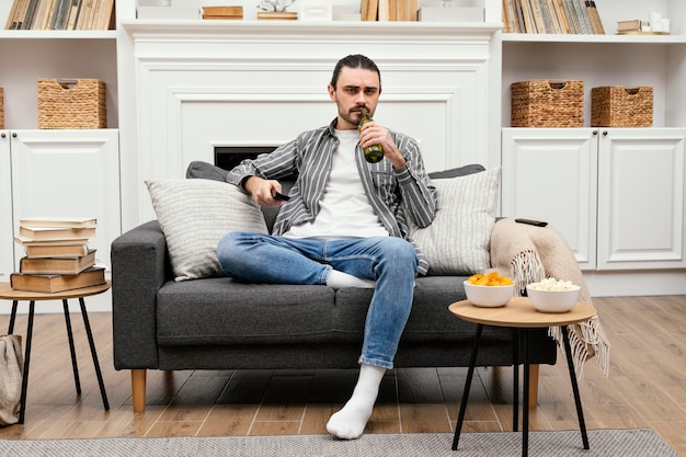 Hombre disfrutando de una cerveza y viendo la televisión sentado en el sofá