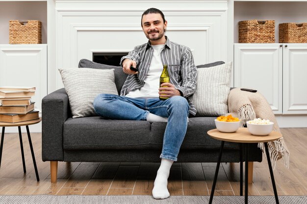 Hombre disfrutando de una cerveza y viendo la televisión sentado en el sofá