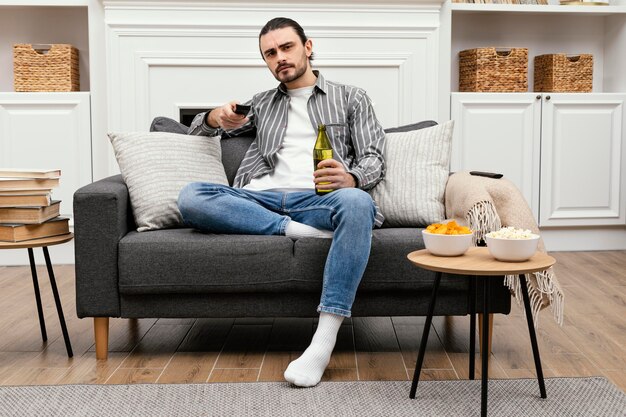 Hombre disfrutando de una cerveza y viendo la televisión tiro largo