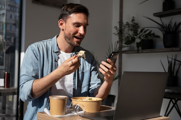 Hombre disfrutando de comida para llevar y con smartphone