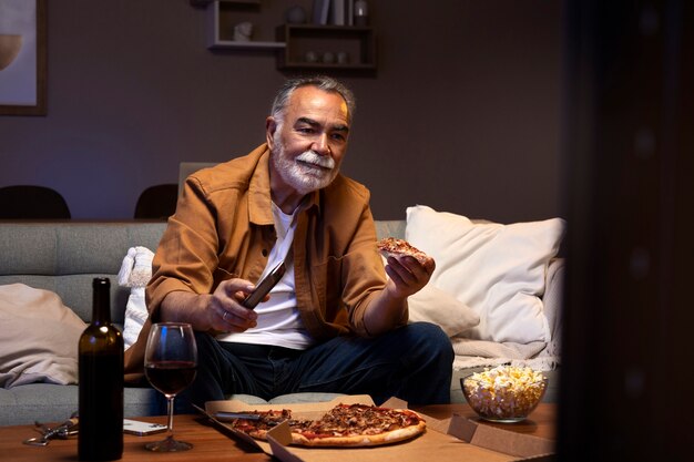 Hombre disfrutando de la comida mientras está solo en casa y ve la televisión