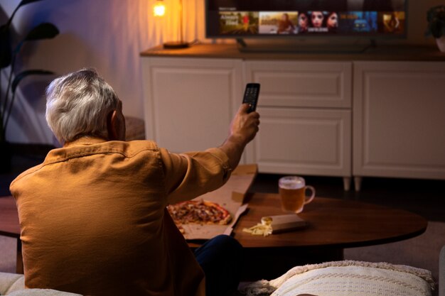 Hombre disfrutando de la comida mientras está solo en casa y ve la televisión