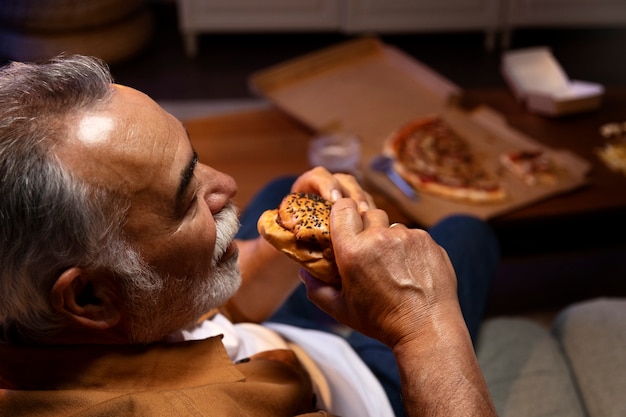 Hombre disfrutando de una hamburguesa mientras está solo en casa