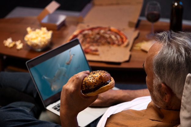 Hombre disfrutando de una hamburguesa mientras está solo en casa