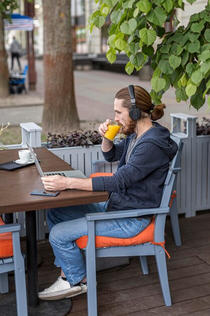 Hombre disfrutando de jugo en una terraza de la ciudad mientras trabajaba en la computadora portátil